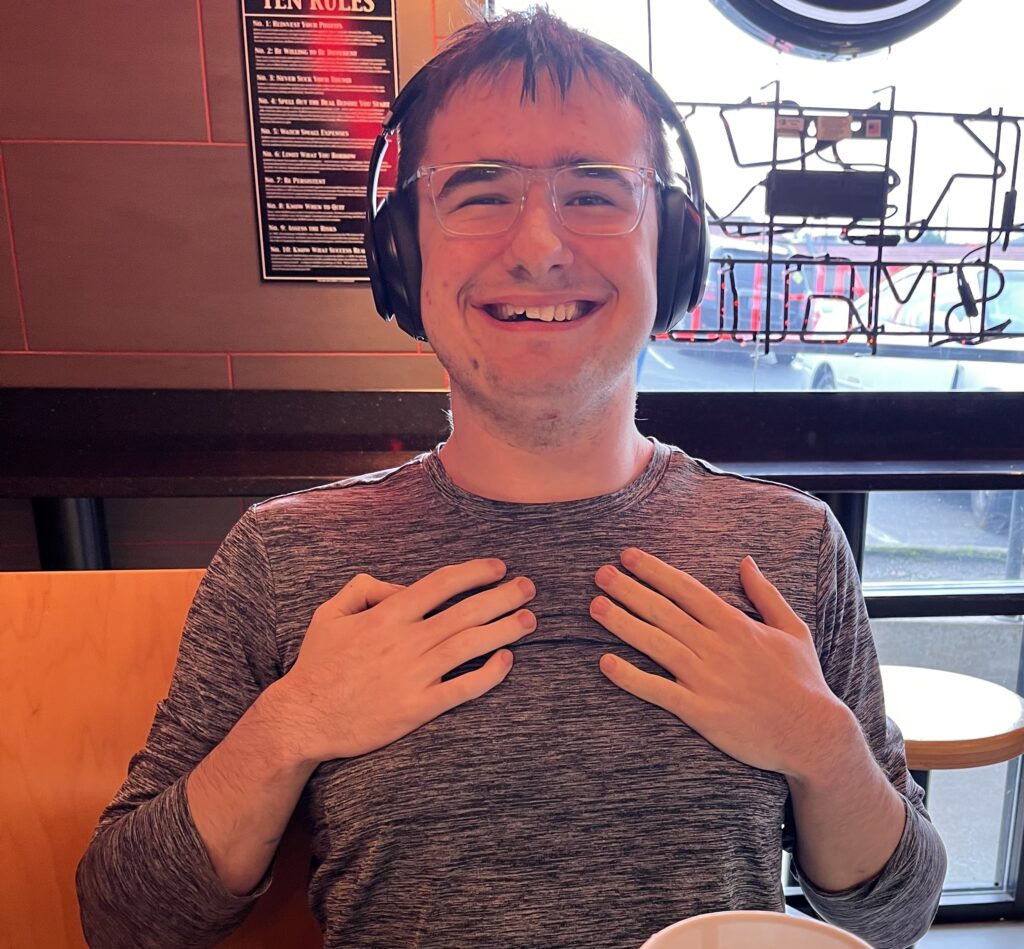 Young autistic man wearing headphone smiling proudly while eating a sandwich at a fast food restaurant.