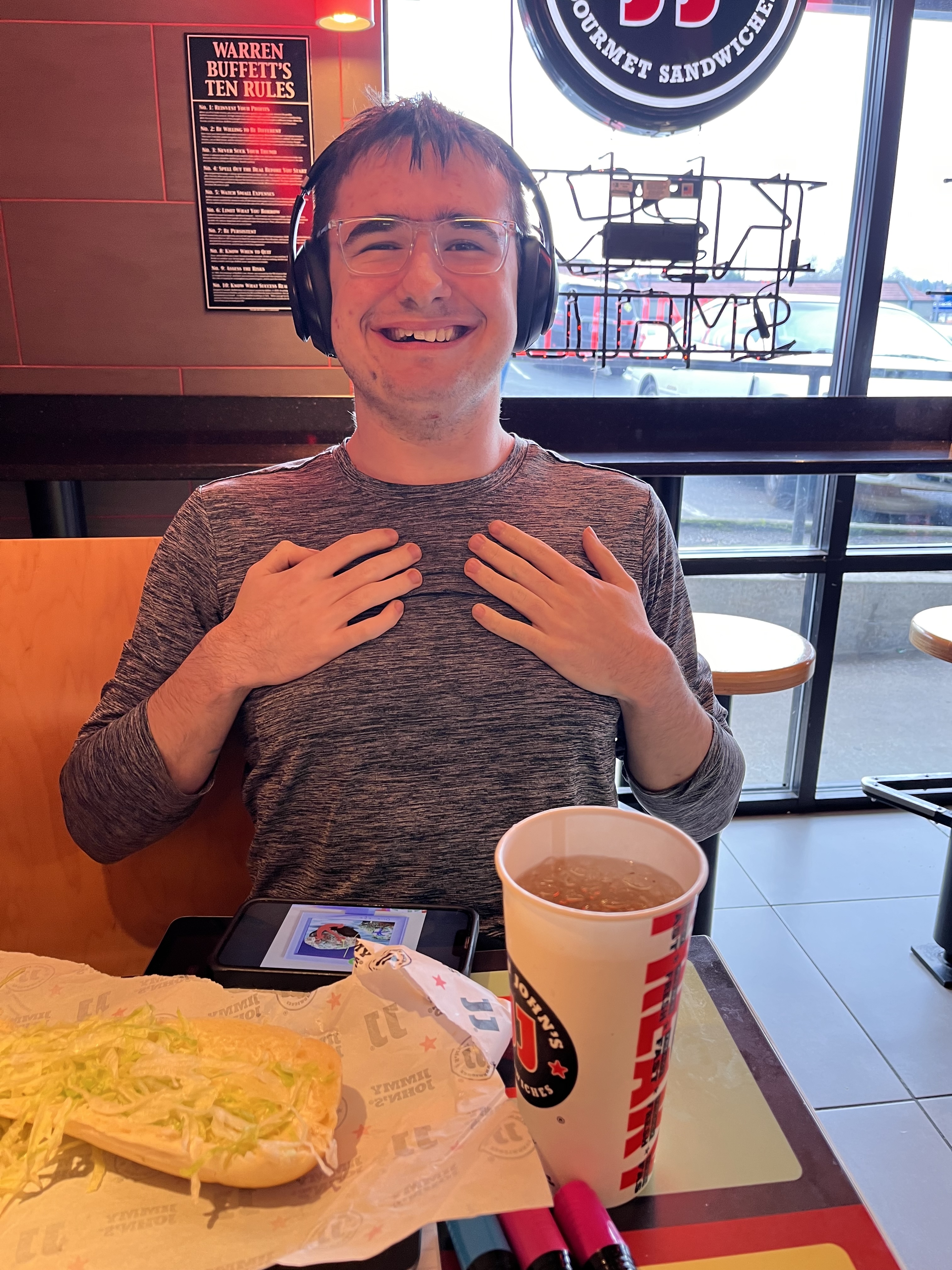 Young autistic man wearing headphone smiling proudly while eating a sandwich at a fast food restaurant.