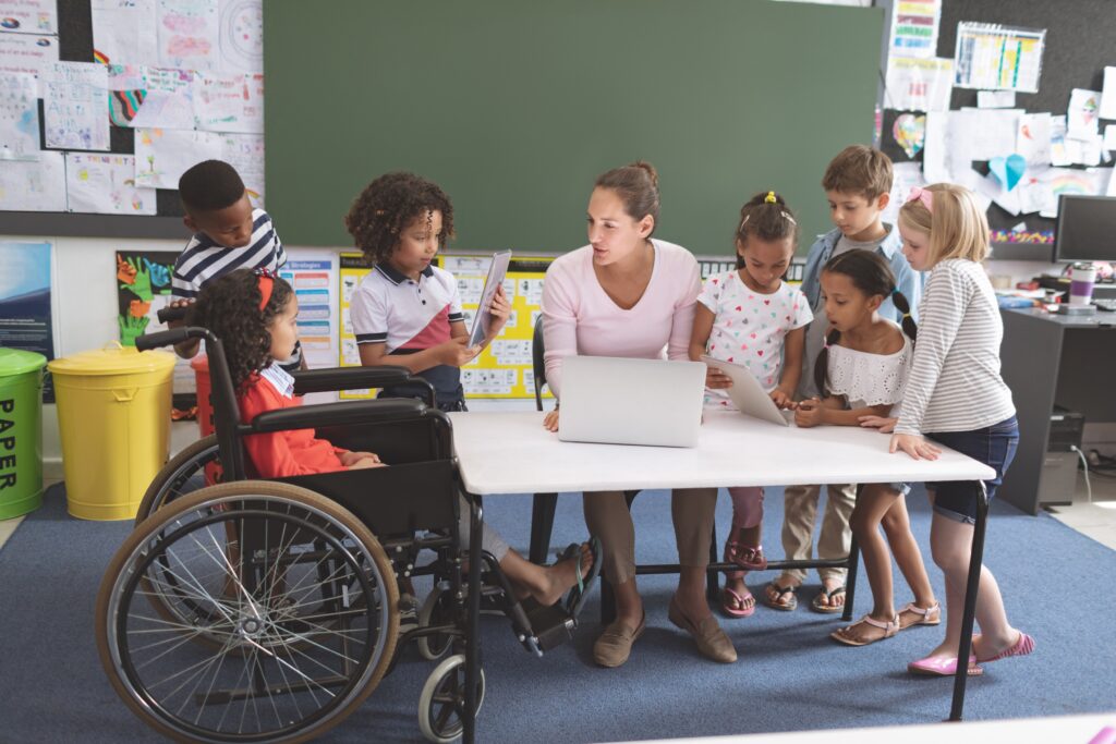 Group of students of different abilities surround a teacher in the classroom.