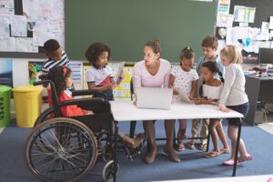 Group of students of different abilities surround a teacher in the classroom.